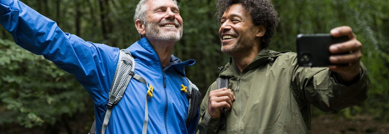 Older man and his grown up son taking a smiling selfie on a walk in the woods