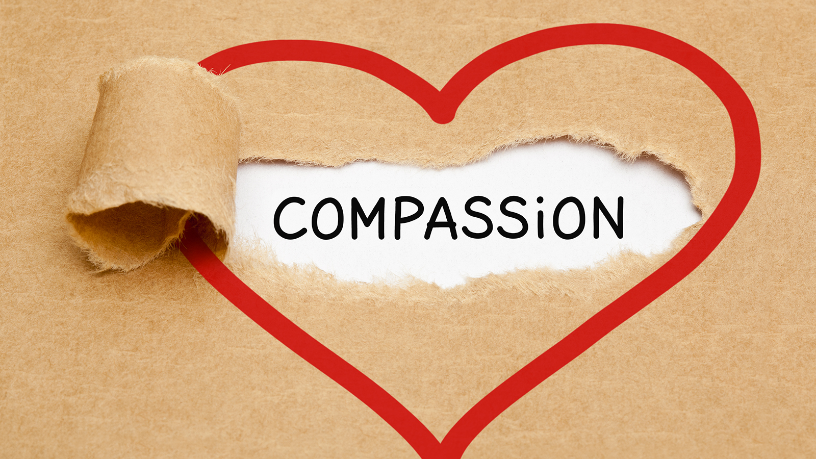 red heart drawn on brown paper torn to reveal the word compassion