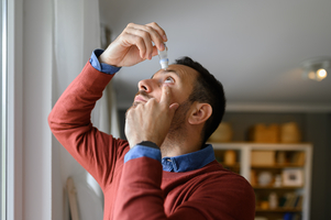 Man wearing red jumper putting in eye drops
