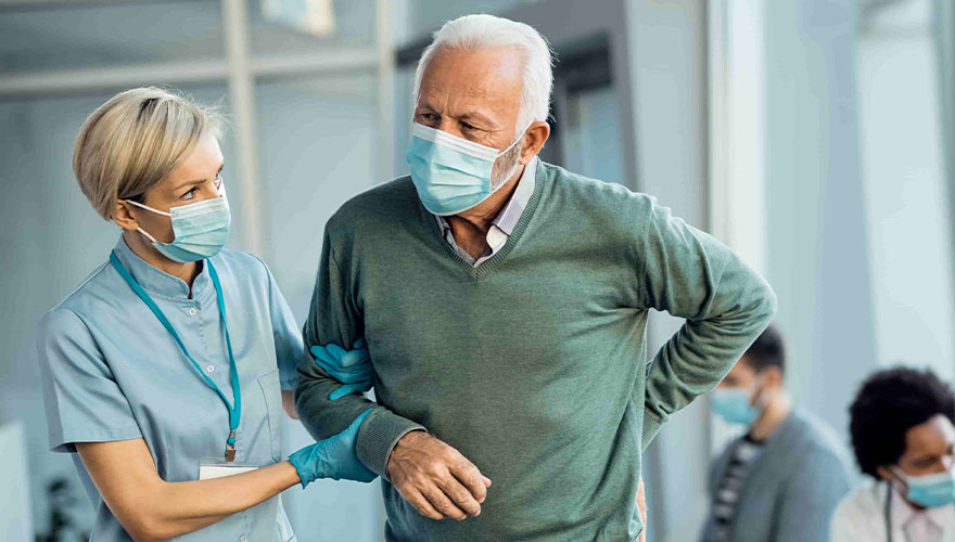 female nurse holding onto mans arm and helping him walk as he holds his back in pain