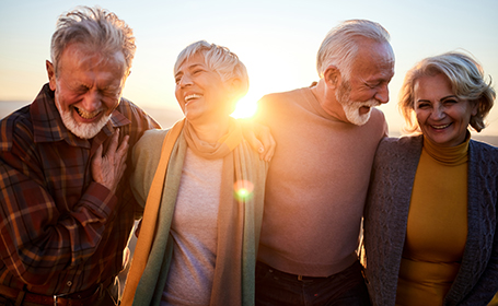 four older people looking very happy on a walk at sunset