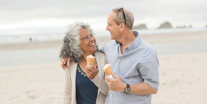 middle aged couple walking carefree on the beach with ice creams