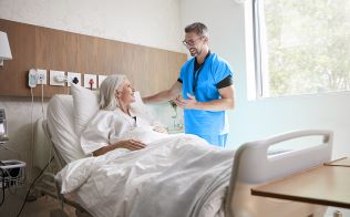 Senior female patient in hospital bed talking to male in blue scrubs