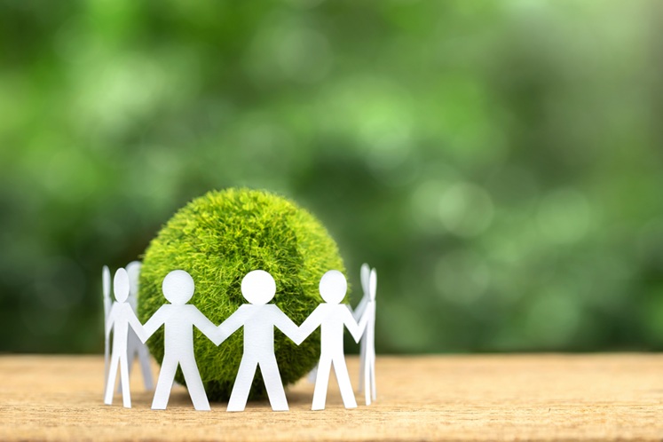 Paper people holding hands standing around a green earth