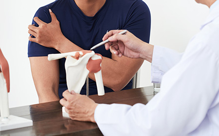 Consultant showing model of bone to patient who is suffering from pain in his shoulder