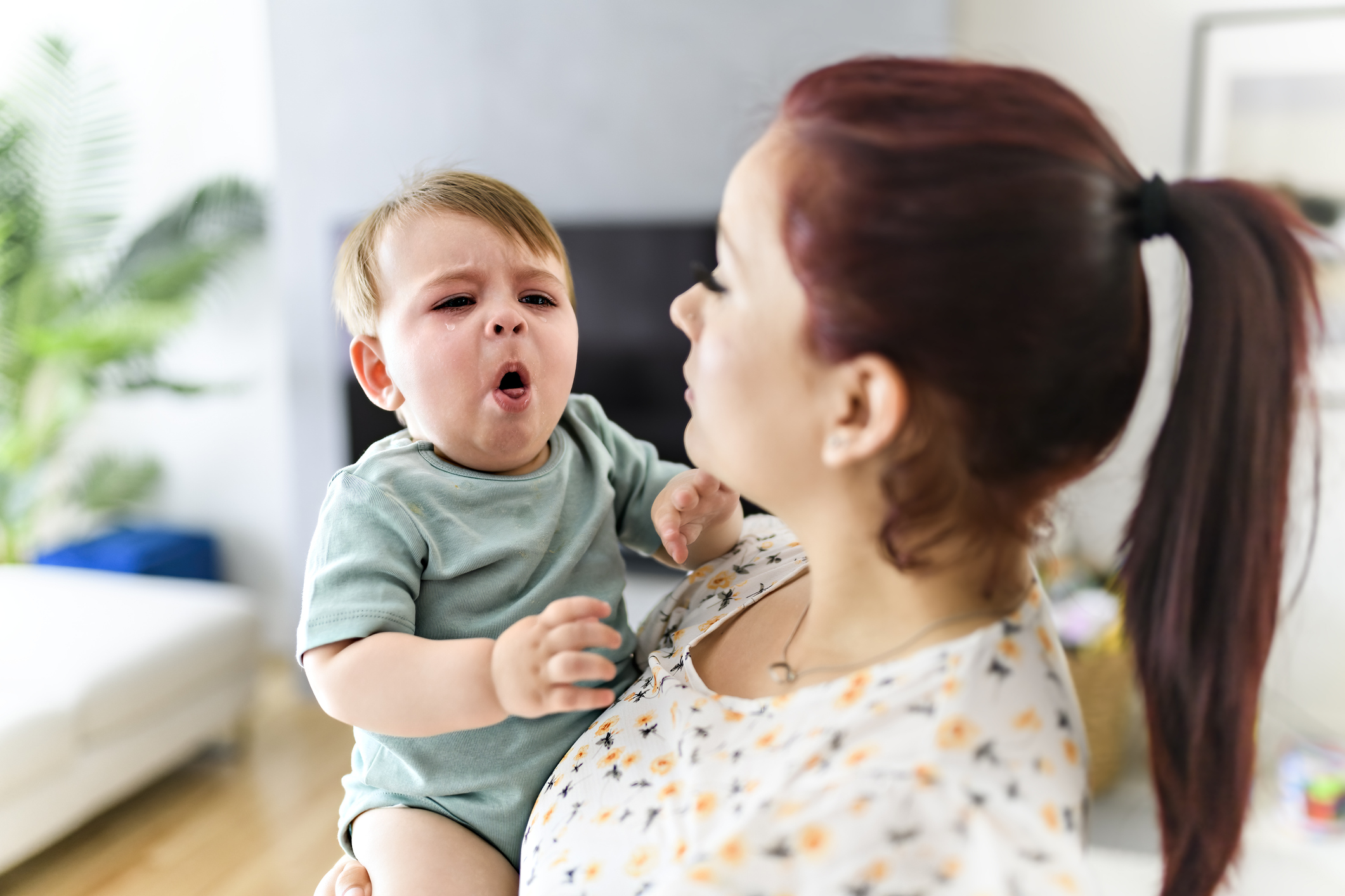 A young child is coughing while being held by its mother