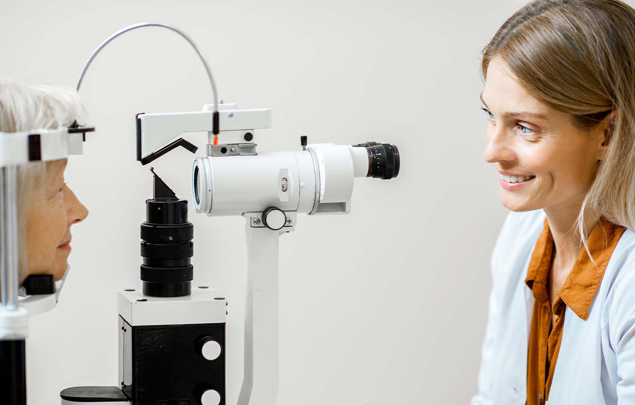Cheerful ophthalmologist examining eyes of a senior patient using microscope during a medical examination