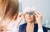 Optician doctor examining elder woman's eye using a trial frame
