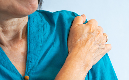 A patient with frozen shoulder holds her arm in discomfort