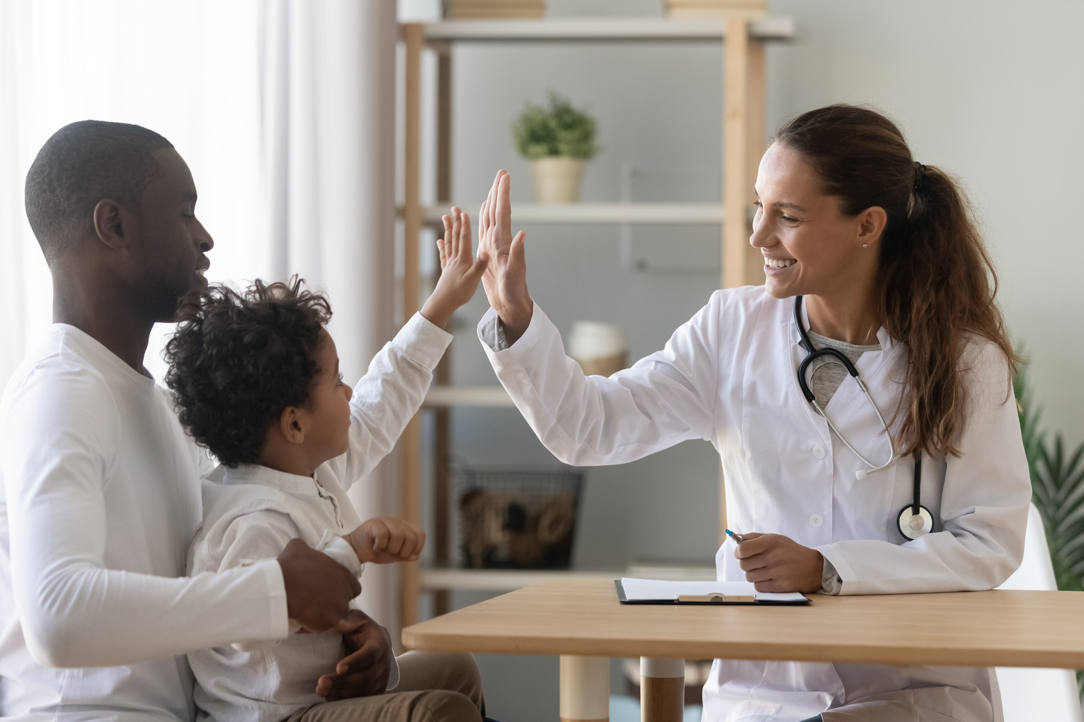 A young boy with his dad is high-fiving a female doctor