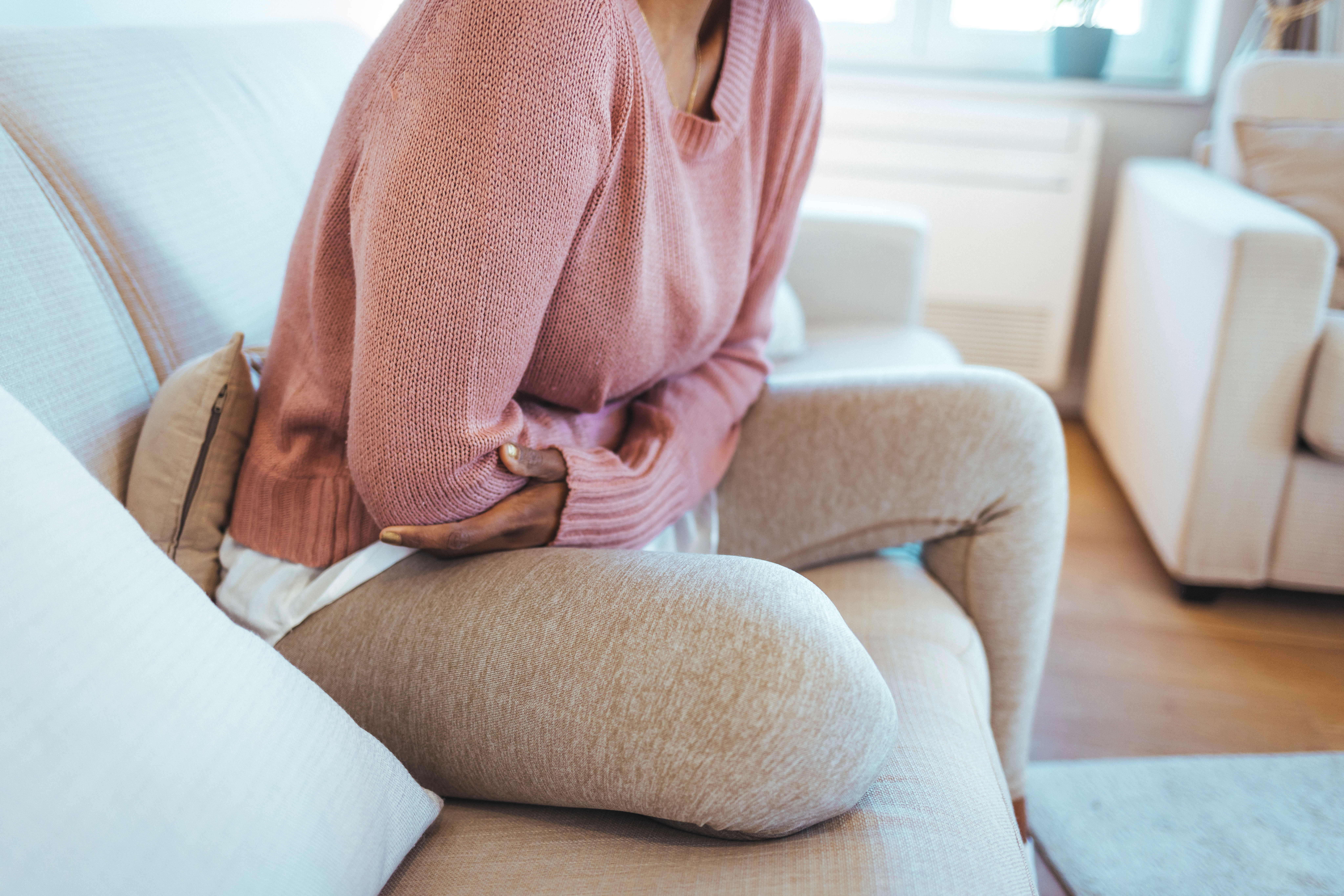 A young woman sat on the sofa and suffering from abdominal pains