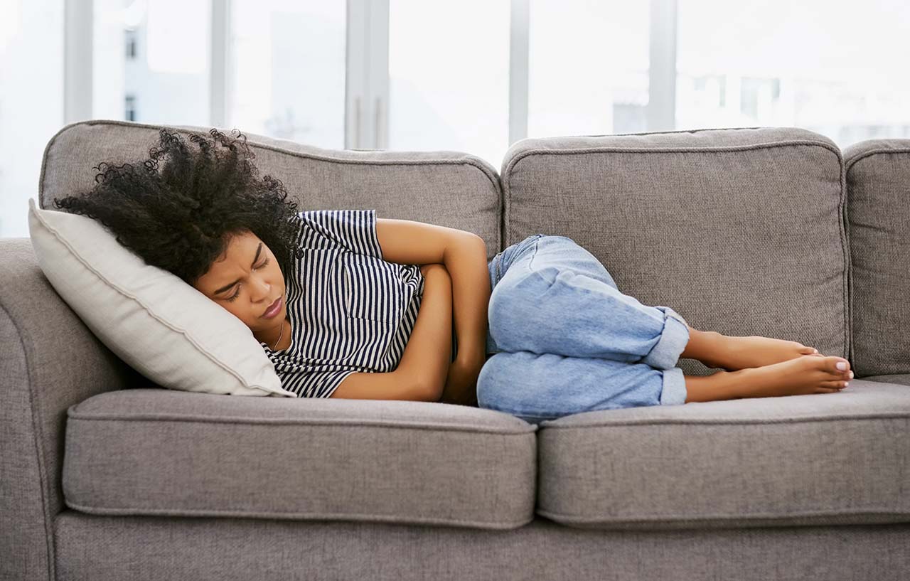 Woman with heavy periods is lying on the sofa with stomach cramps caused by menorrhagia