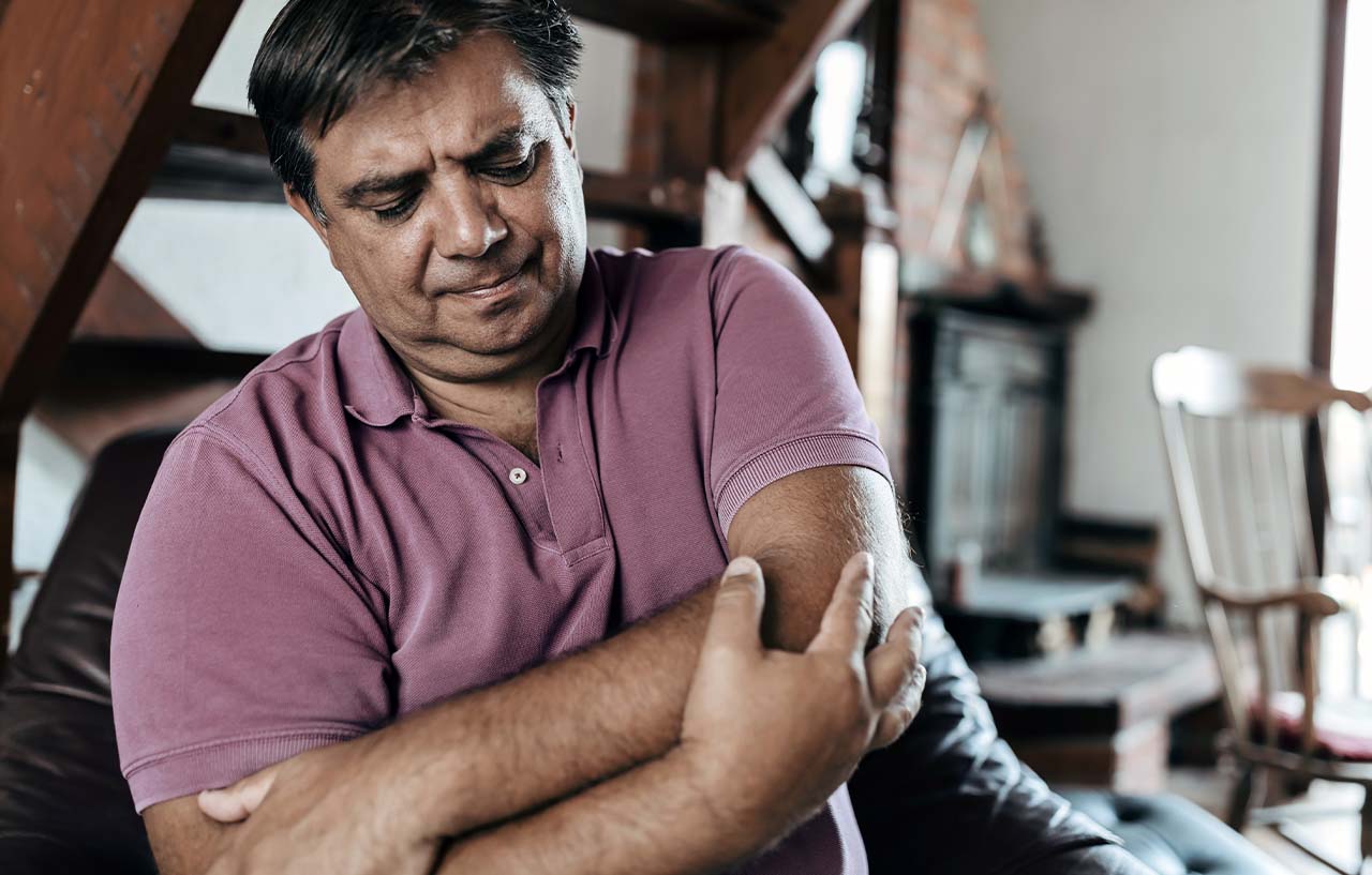 Man needing golfer's elbow treatment holds his arm in discomfort
