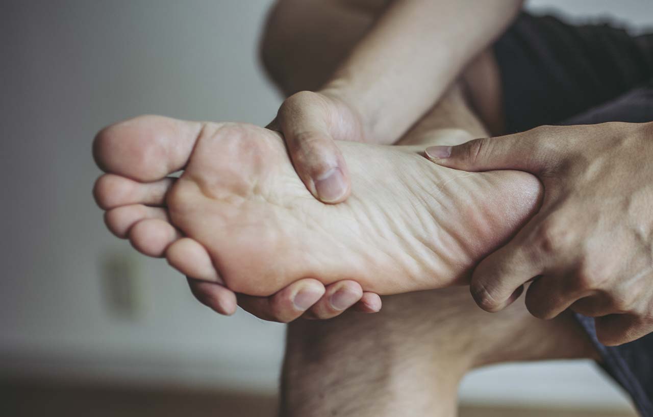 Man holding onto his feet and showing parts of his foot that are in pain
