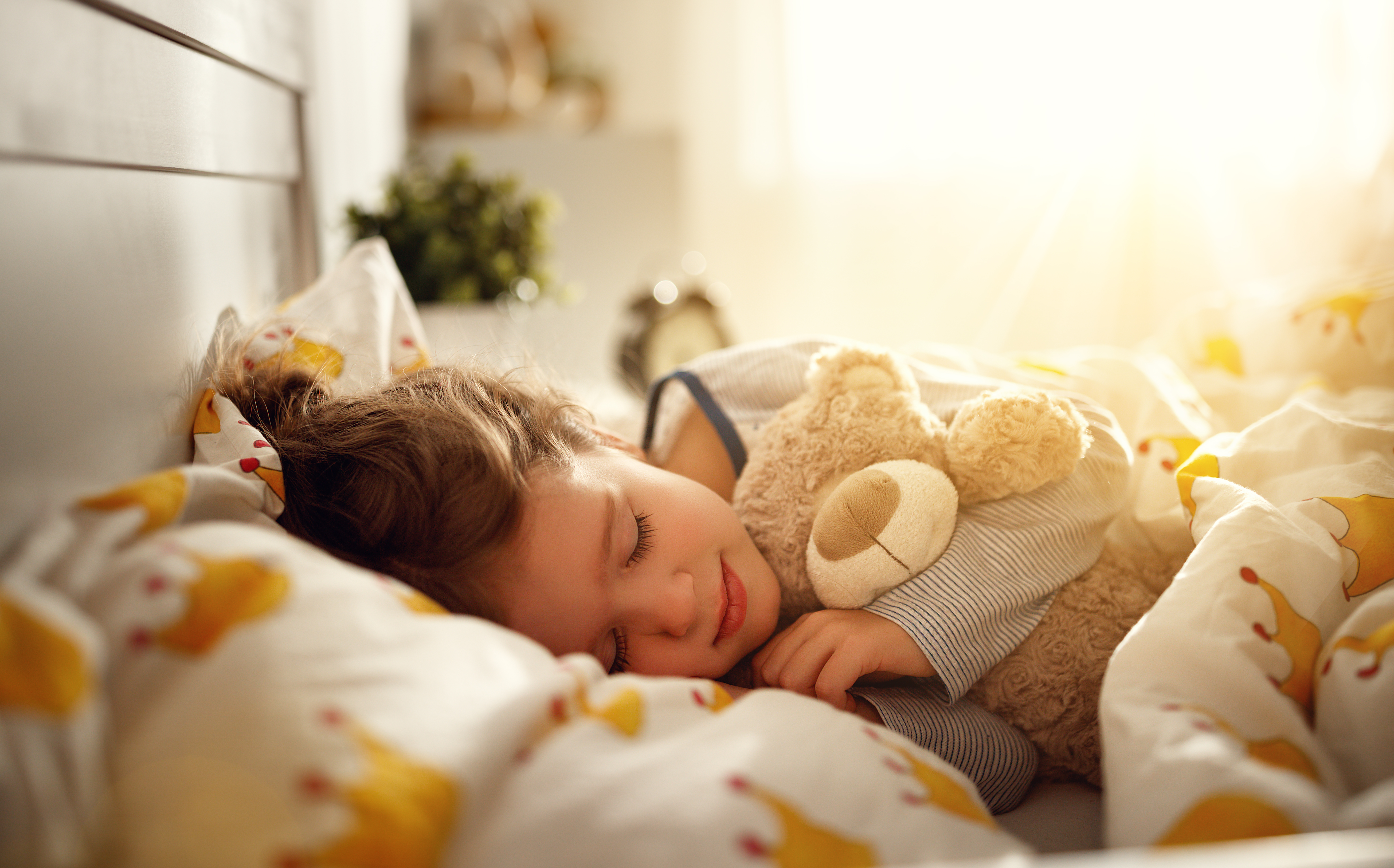 A child asleep in bed holding a teddy bear