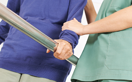 clinician holding hands of elder patient holding onto to walking aid