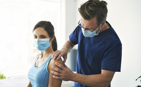 masked clinican and patient in consultation, performing physical assessments