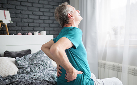 elder man getting out of bed with hands on his back in pain