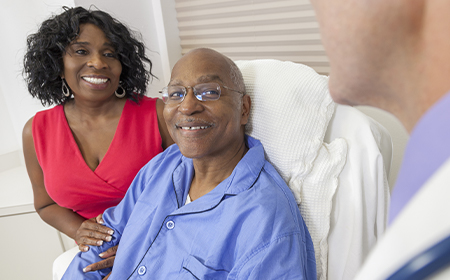 elder male led in hospital bed with his wife stood next to him whilst talking to doctor