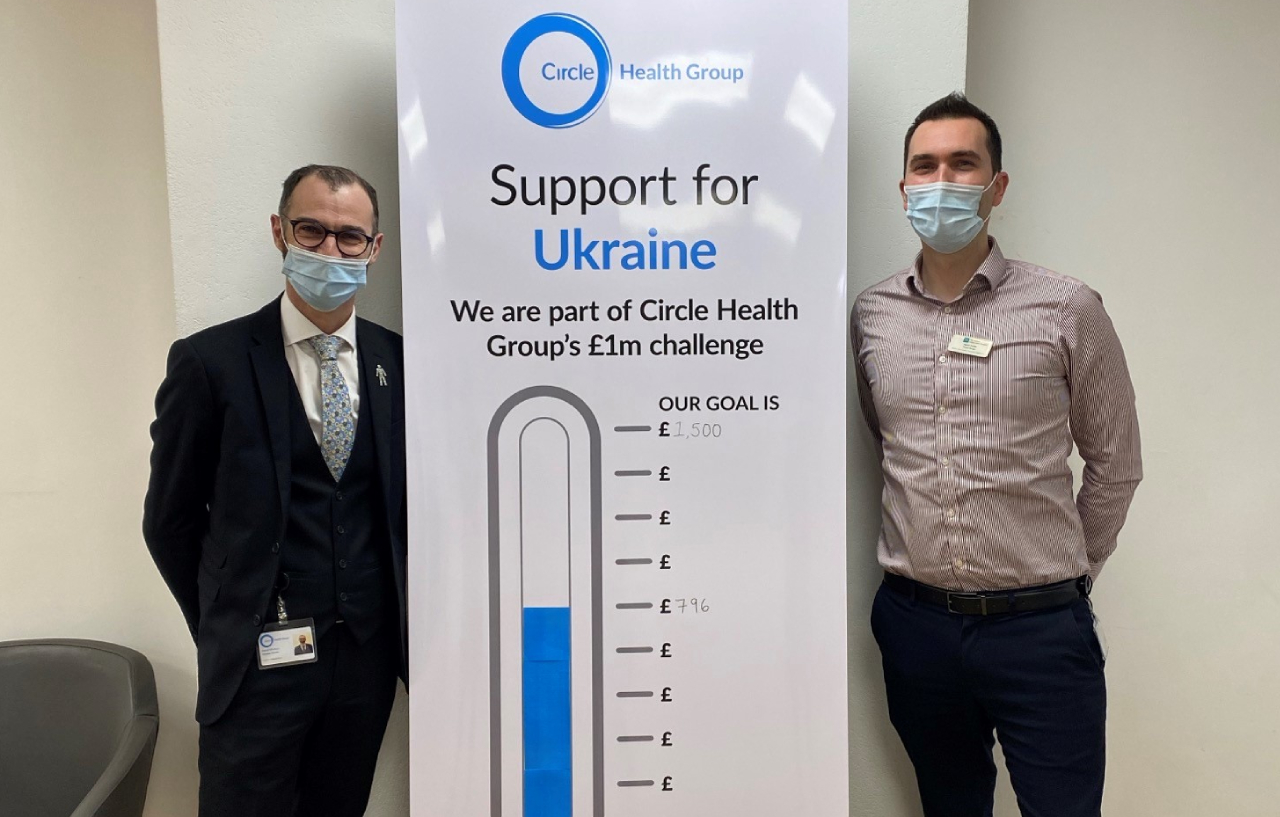 Two employees pose by a support Ukraine poster